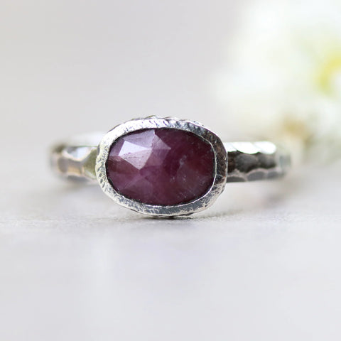A silver ring featuring a rectangular faceted ruby gemstone set in a silver bezel setting, complemented by a sterling silver oxidized hard-textured band, creating a unique and stylish piece of jewelry.