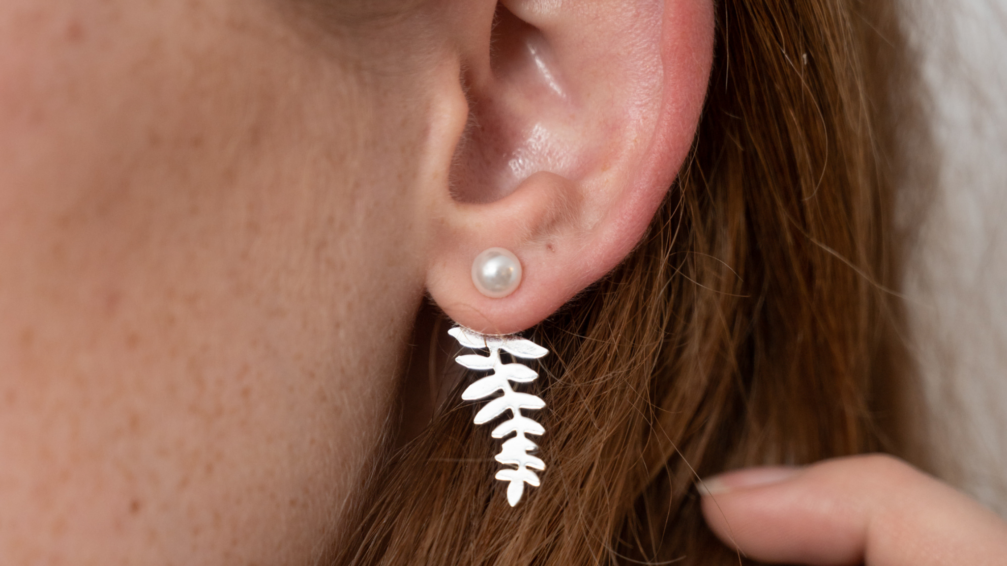 Close up of woman's ear wearing a pearl and silver leaf ear jacket.