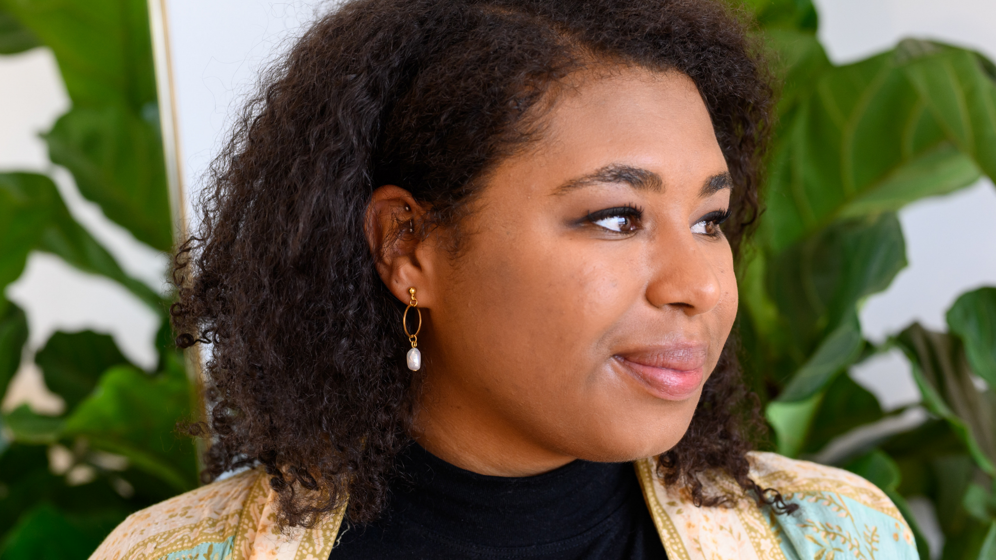 The side profile of a young black women wearing pearl hoop earrings.