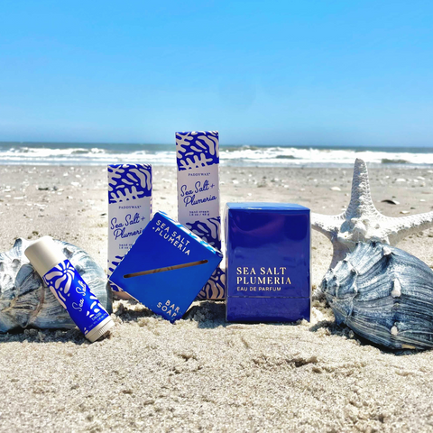 Paddywax Body products in blue packaging on sandy beach with sea shells surrounding them