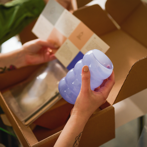 Person opening up candle making kit and holding a blue candle jar and instructions on how to make scented candle