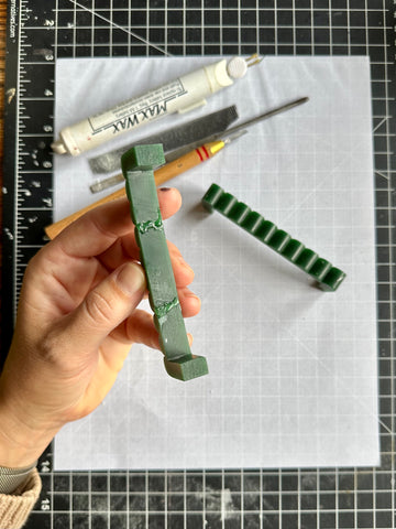 a hand carved wax models being help in a hand on a studio table