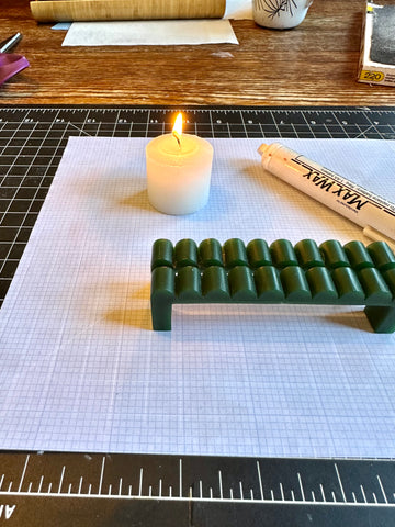 two hand carved green wax models on a work table with a wax pen and candle