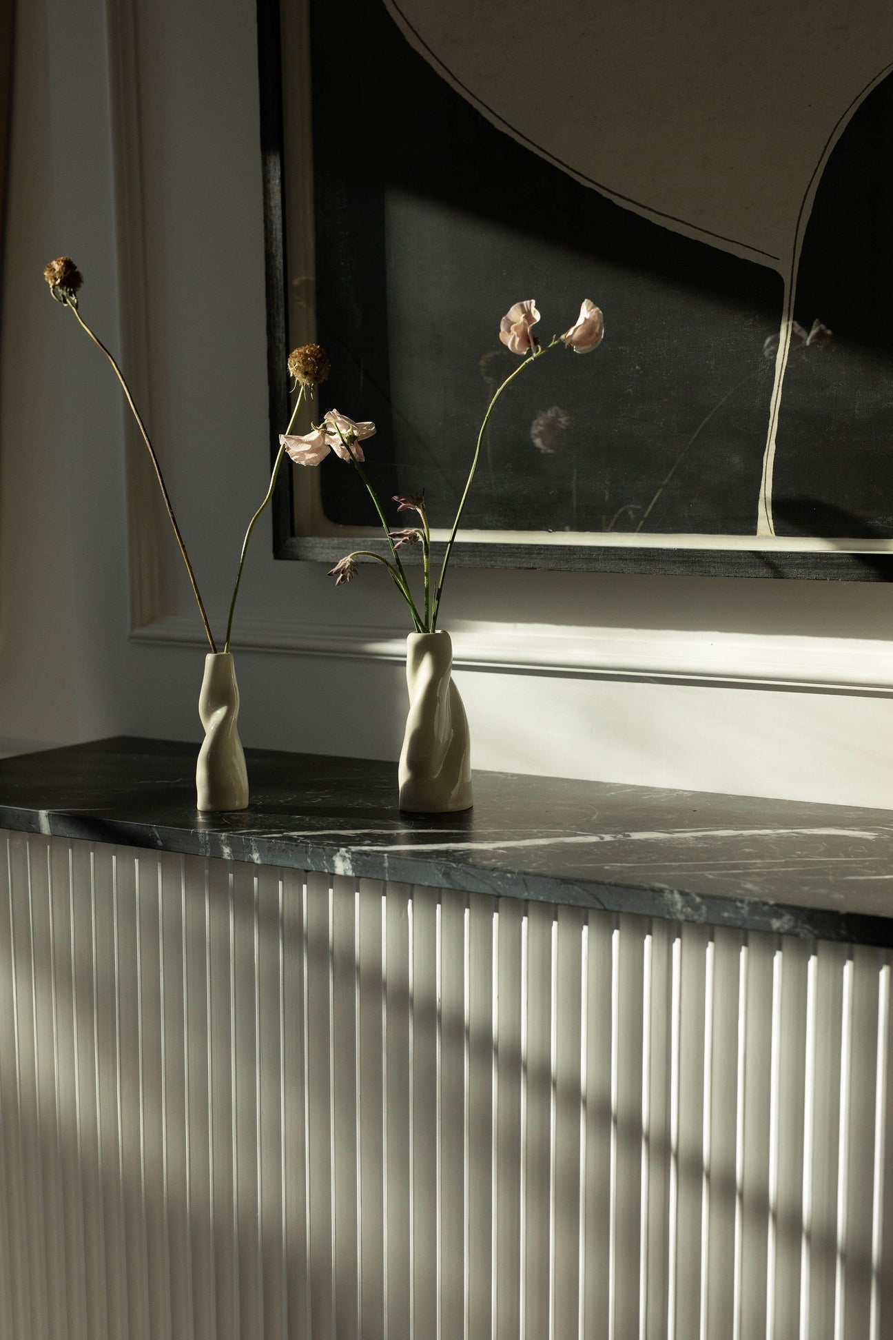 two abstract vases holding fresh flowers on top of a dark marble mantle