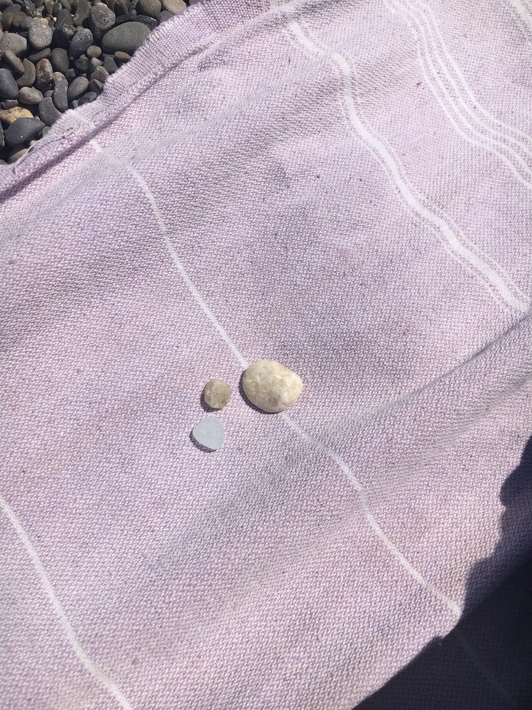 some rocks and sea glass on a pink beach blanket