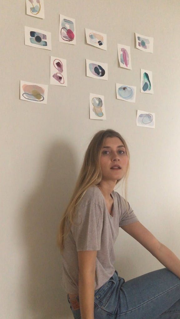 artist sitting in front of the small work pinned on a wall