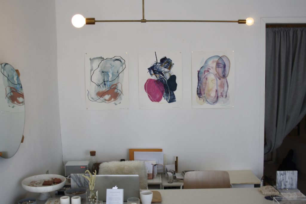 a row of three larger paintings hanging behind a desk 