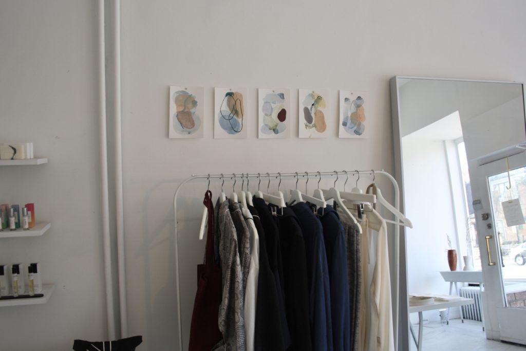 a row of abstract studies hanging above a rack of clothes 