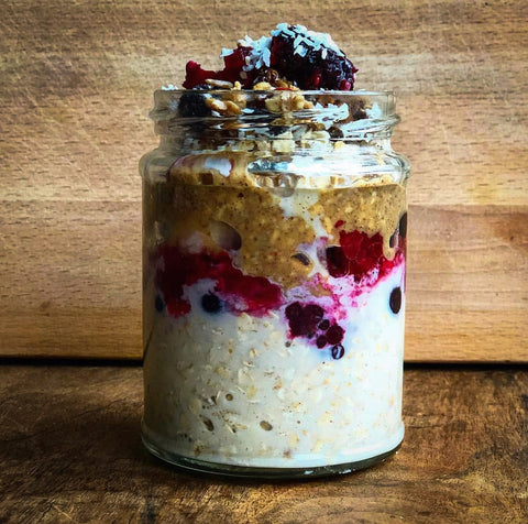 A Pinterest-worthy mason jar filled with Gem's delicious, simple overnight oats recipe. The jar is layered with oats, frozen purple and red berries, and topped with fresh berries and desiccated coconut.