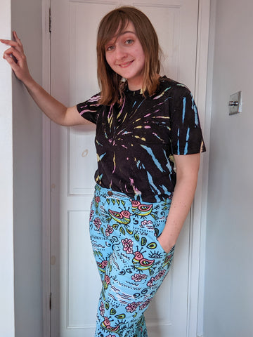 Cheryl is standing in a doorway, wearing a Black tie-dyed top and patterned trousers