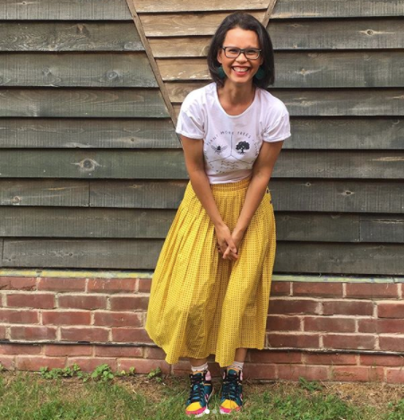 Jamie the Unwedding Wedding Expert, smiling by a barn in a yellow dress, white top and fun colourful trainers