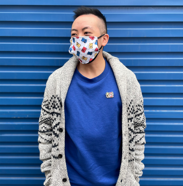 Image of Euge Leung standing in front of a blue container wearing a Gummie Puglie patterned mask, and a White Rabbit Puglie Pin on a blue sweater.
