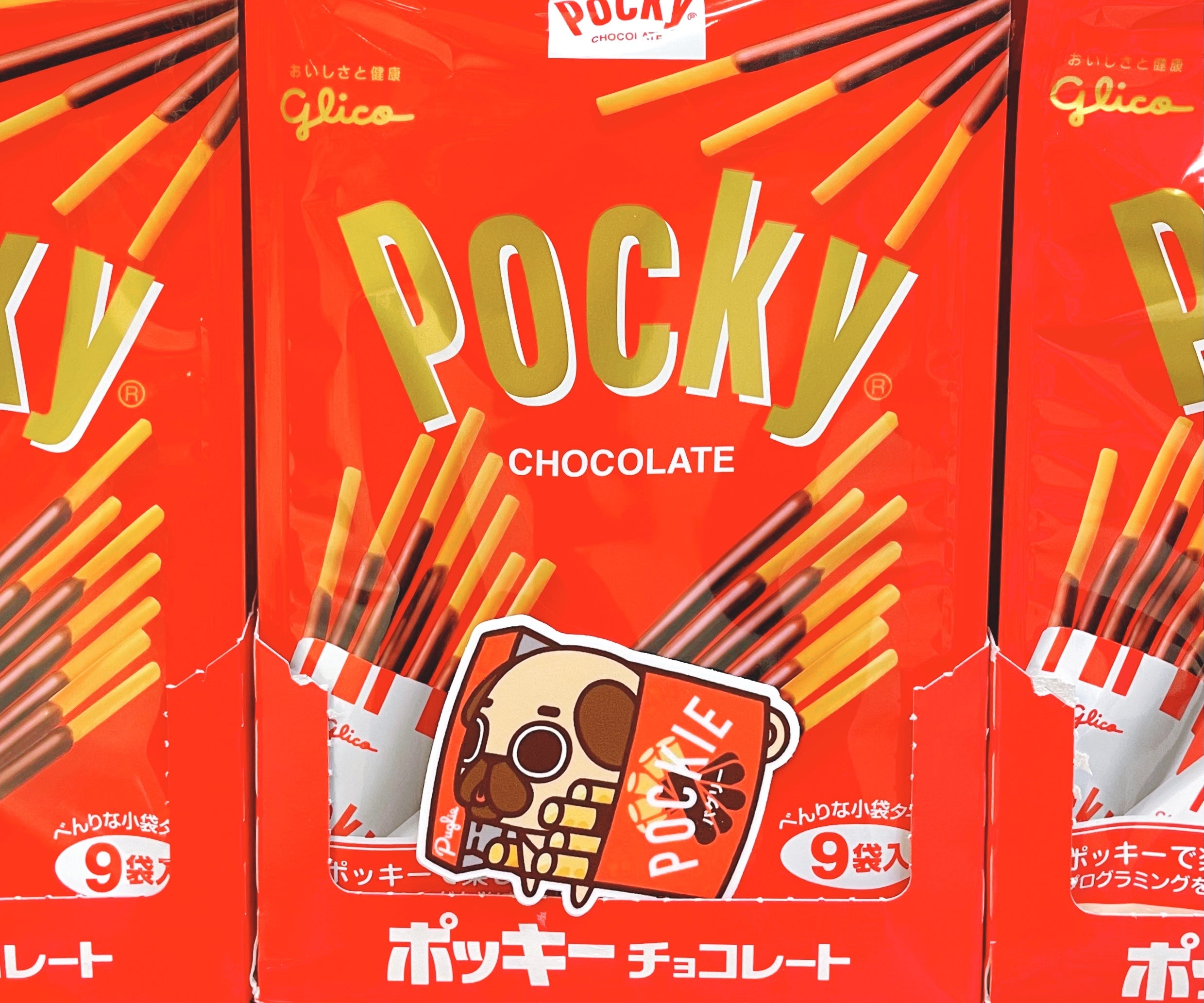 Puglie Chocolate Pocky Sticker posing in front of red Chocolate Pocky packaging