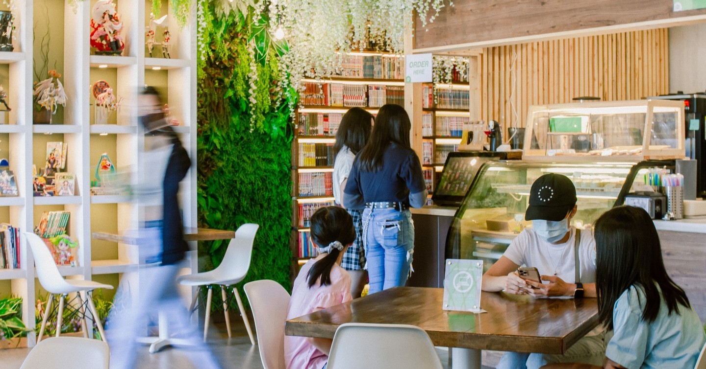 View of wall shelves with anime figurines and the cashier counter with hanging leaves along the walls.