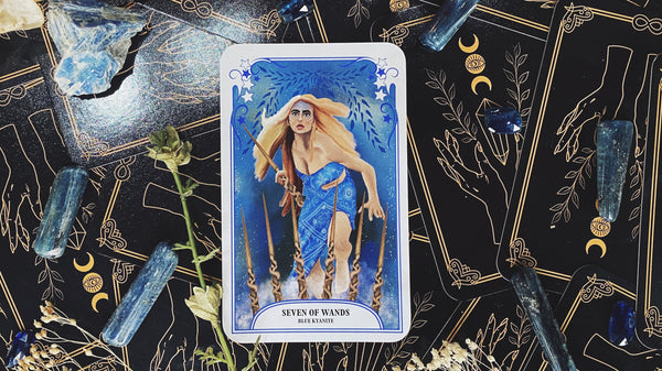 Seven of wands tarot card meaning with blue kyanite crystal. warrior woman in a blue dress holding a wand like a sword.