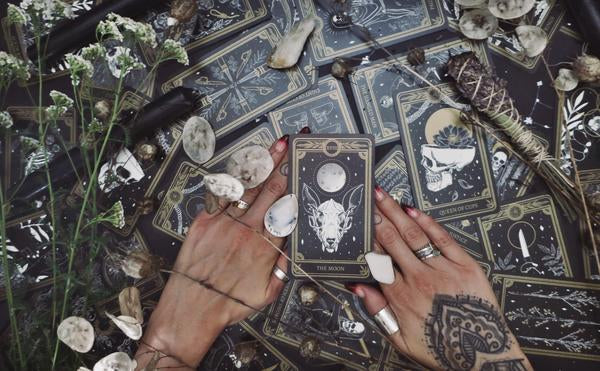 black and white tarot cards spread out with hands on top and the card, The Moon centred