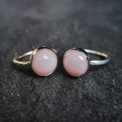 two pastel pink opal rings side by side with round stones, one se tin silver, one in 9ct gold, on a dark grey granite background