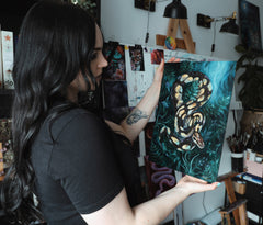 Artist Live Vilemsone in her studio holding up an oil painting of a snake