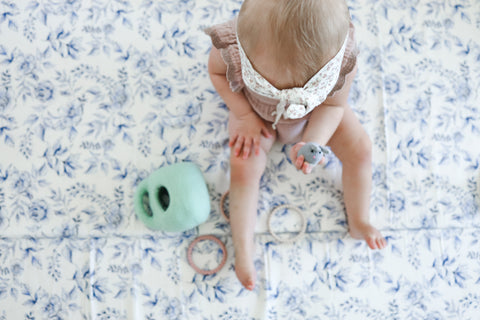 toddler sitting on a blue florals and stripes toki mat