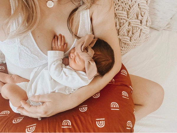 mom cradling a newborn, using a nursing pillow by toki mats