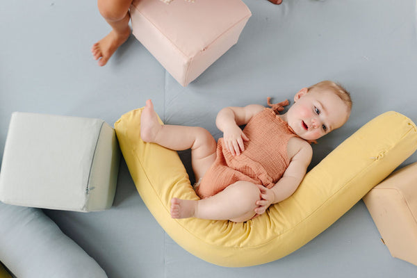 toddler laying on a toki mats play mat and surrounded by a support pillow and play cubes