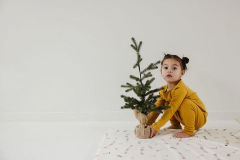 toddler girl sitting on a toki mats play mat with a small fir tree