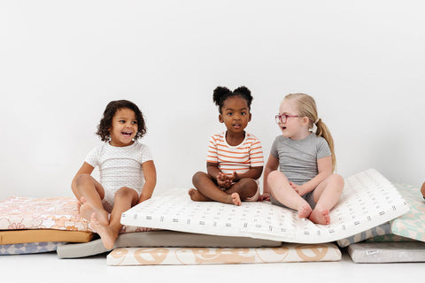 three children sitting on a stack of toki mats play cushions