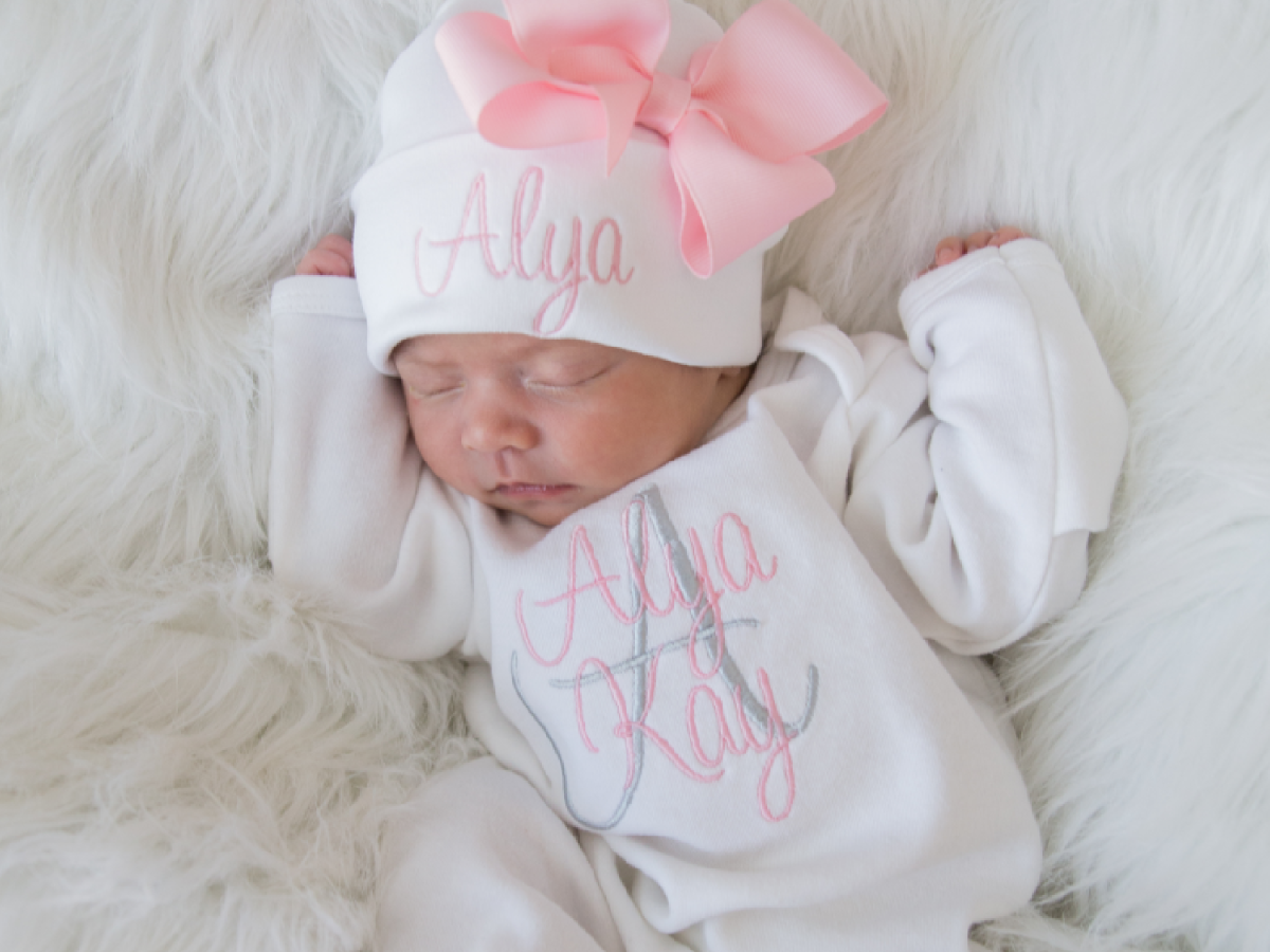 A baby in a monogrammed white bodysuit with pink headband.