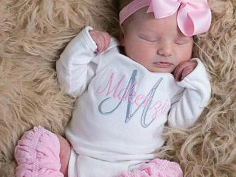 Sleeping baby in personalized outfit with pink leg warmers and bow.