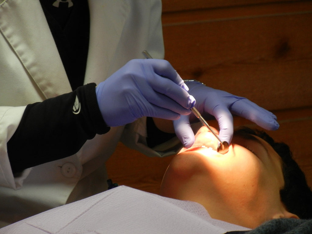 Dentist with protective gloves and sterilized tools examining a patient’s mouth