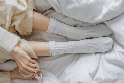 Person sitting in bed holding a cup and wearing white socks