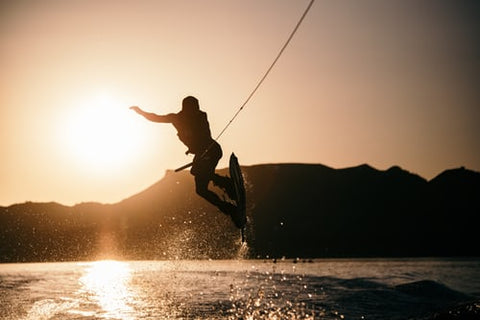 silhouette of person jumping off water while wakeboarding at sunset
