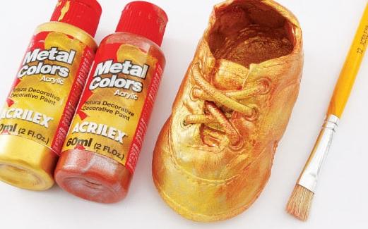 brush and metallic paints next to bronzed baby shoes