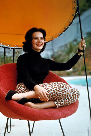 Vintage 1950s young woman wearing leopard print capri pants and black turtleneck jumper sat by a pool