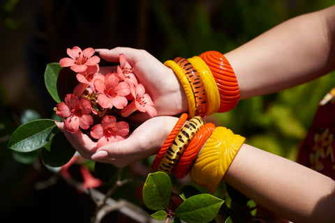 Splendette vintage inspired 1950s orange and yellow bangles worn by model holding tropical flowers