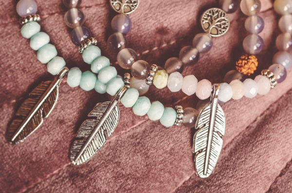 three beaded bracelets, each with a single, silver, feather-shaped metal charm