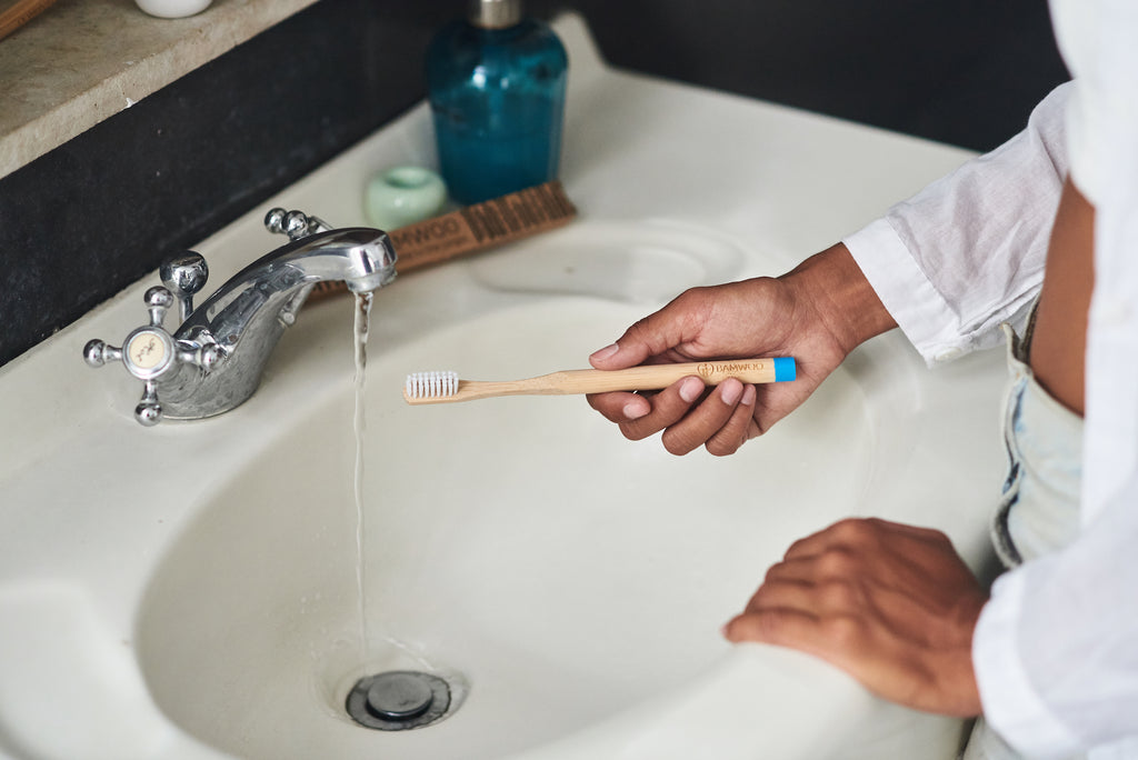 Girl holding a BAMWOO bamboo toothbrush over a sink with running water
