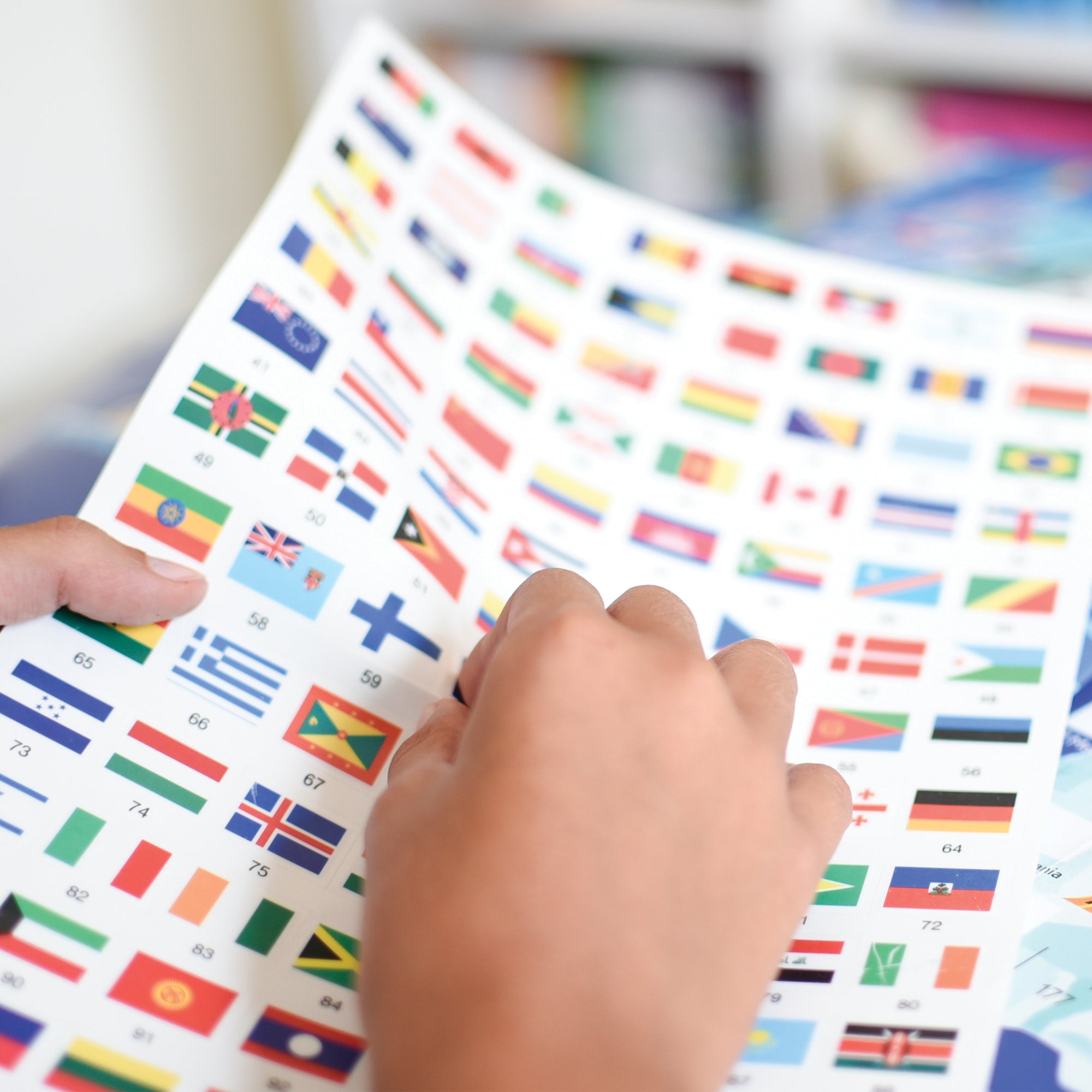 The hand of a child pulling up a flag sticker from a sheet of flag stickers. The backround is out of focus.