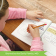 A customer photo of a girl in a pink fuzzy sweater sitting at a table drawing in the 101 Doodle Definitions  book. On the left page, you can see her drawing a hierarchy. On the right page you can see some Egyptian hieroglyphics.