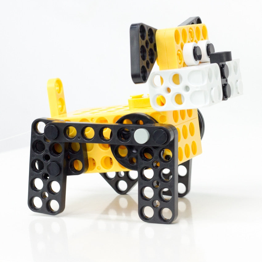 Robotis Play 600 Pet dog robot in the process of walking. Dog face and body are yellow and the legs, eyes, nose, and ears are black with some white accents.