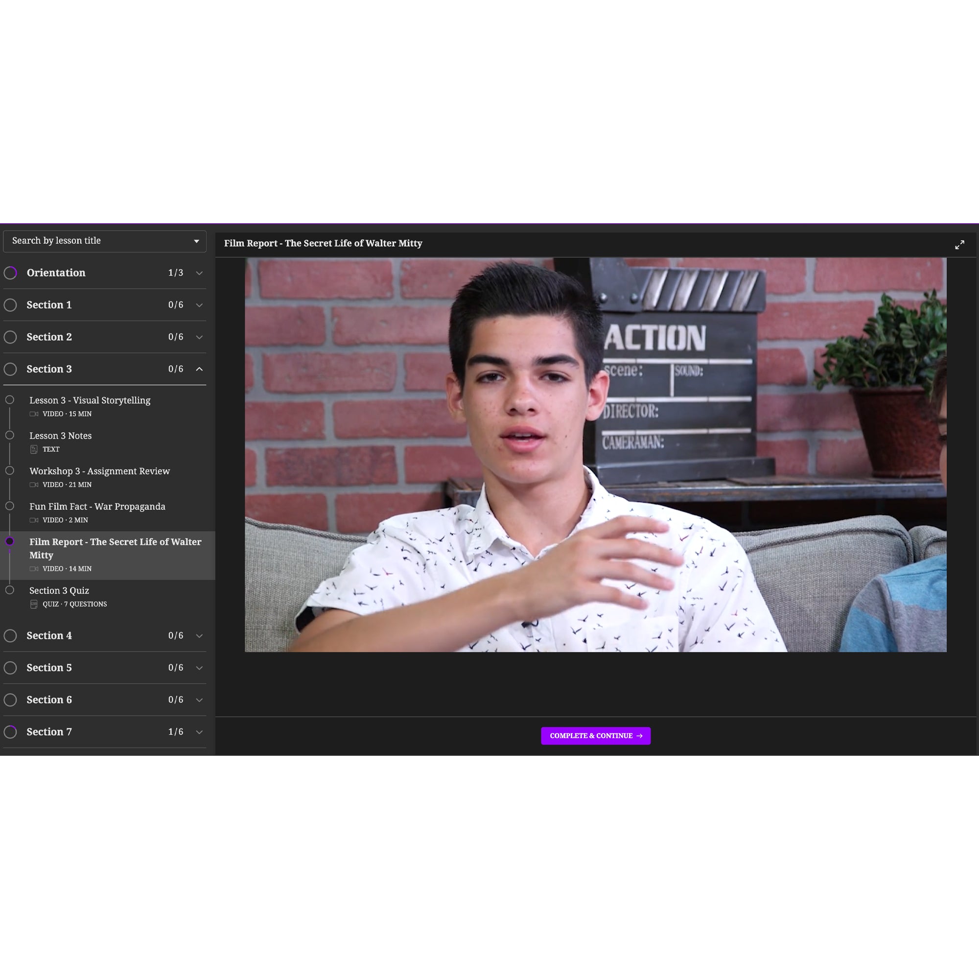 A screenshot of the Intro to Filmmaking program. There is a menu on the left and the background is a dark gray and black with a bright purple button at the bottom. The middle of the screen shows a teenage boy sitting on a couch in the middle of talking with his right hand up and to his left. Behind him is a brick wall and a clapperboard and potted plant for décor.