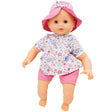 Corolle’s Bebe Coralie. The light skinned baby doll has brown blinkable eyes. She is wearing pink shorts and a floral shirt with a variety of pinks and periwinkle colored flowers in different sizes. She is wearing a pink hat that has a bow in the middle that matches the shirt print.