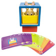 Bunny Boo game contents. The colorful challenge cards are fanned out along the bottom. Behind are the wooden block pieces stacked to match the top card in the challenge card pile. Inside the hollow blue piece is the bunny piece that is inside a yellow piece that has a circle cut out in the middle. These pieces are set on top of a red block piece.