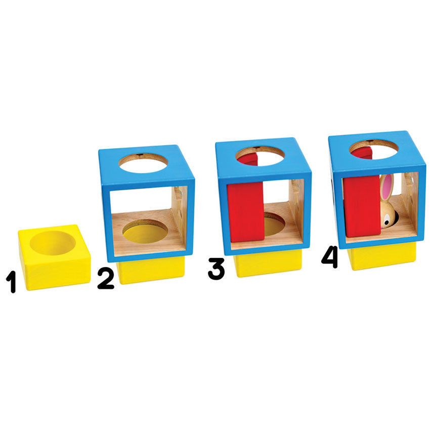 The Bunny Boo game showing steps of putting the blocks in place to fulfill a challenge. Step 1 shows a yellow block with a circle cut out in the middle. Step 2 shows a hollow blue block with shapes cut out on the side stacked on top of the yellow block. Step 3 shows a red block tucked inside the blue block. Step 4 shows the bunny placed inside the blue block and tucked behind the red block.