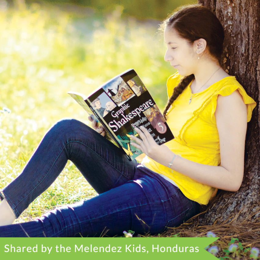 A young dark-haired girl in a yellow shirt and jeans is sitting up against a tree and reading the Graphic Shakespeare book. The cover is mainly black with white text and illustrations of the plays inside. The cover shows that the book includes; Romeo & Juliet, Julius Caesar, Hamlet, Macbeth, and A Midsummer Night’s Dream.