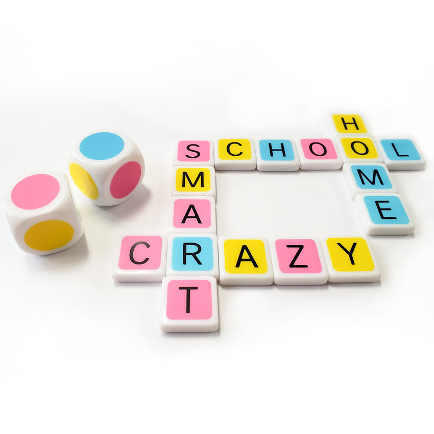 Candygrams game in play. On the left are 2 dice with alternating colored dots on each side, in red, yellow, and blue. To the right of the dice is a crossword made up of the words home, school, crazy, and smart. The letter tiles are pink, yellow, and blue with white sides and backs.