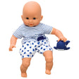 Corolle’s Bebe Marin sitting on a white background. The light skinned baby doll has blue blinkable eyes and is resting his hand on a rubber whale toy to his left. He is wearing shorts and a shirt. His shirt is white with blue stripes and a whale patch on his lower-left. His shorts are white with a blue whale pattern.