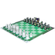 Story Time Chess game board setup up with all the pieces in the starting position. The game board squares are green grass, alternating darker green and lighter green.  The white pieces on the bottom-left side show the standard pieces. They have character cut-outs in front of them, but you are not able to see from this angle, so they are just white cut-outs. On the other side are the black pieces. You can see all the colorful character cut-outs. All pieces are in their starting position.