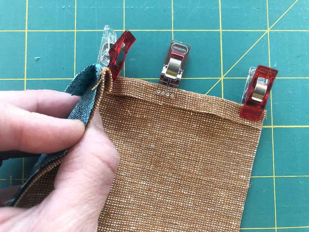 Aligning linen fabrics and securing them with clover clips for hand sewing a flat-felled seam.