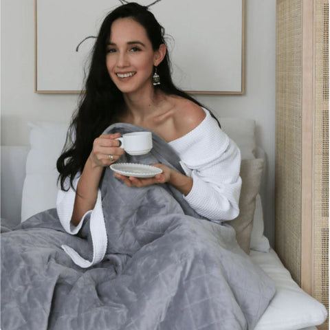 a woman drinking coffee under a weighted blanket